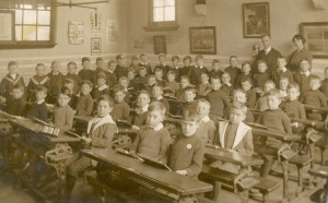 Victorian classroom. Children sat at desks in rows facing the teacher.